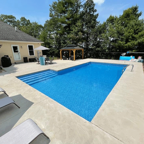 Finished backyard pool project featuring entry steps, concrete patio, and covered gazebo seating area.