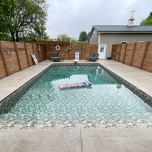 Custom swimming pool with shallow tanning ledge, decorative stone finish, and privacy fencing.