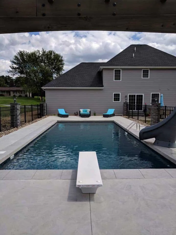 Rectangular in-ground pool with diving board, slide, and modern concrete patio in residential backyard