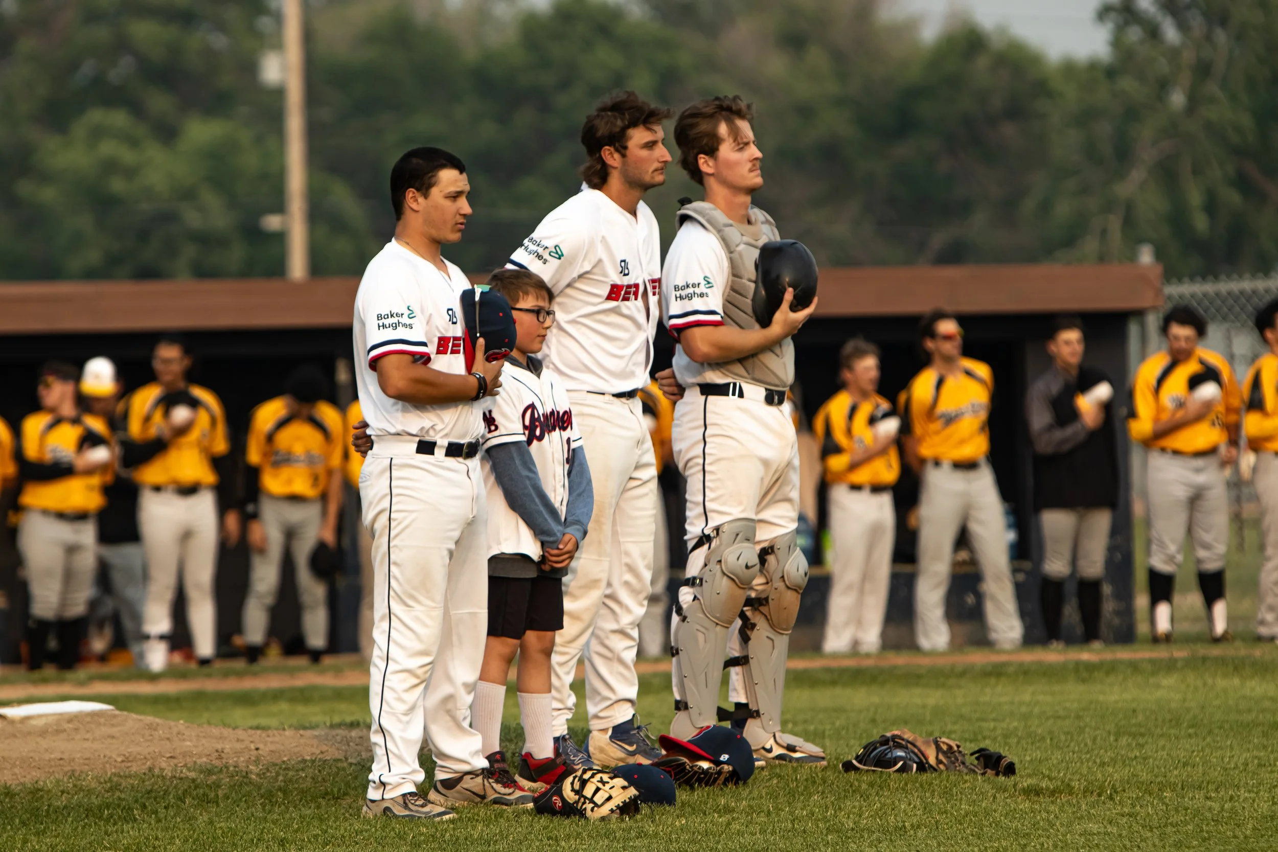 Baseball players and a young fan standing on the field during the national anthem before a game, with players in uniforms and yellow jerseys visible in the background.