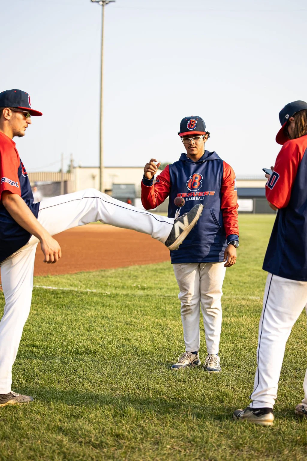 Baseball players warming up on the field, wearing team jackets and hats with a baseball in mid-air