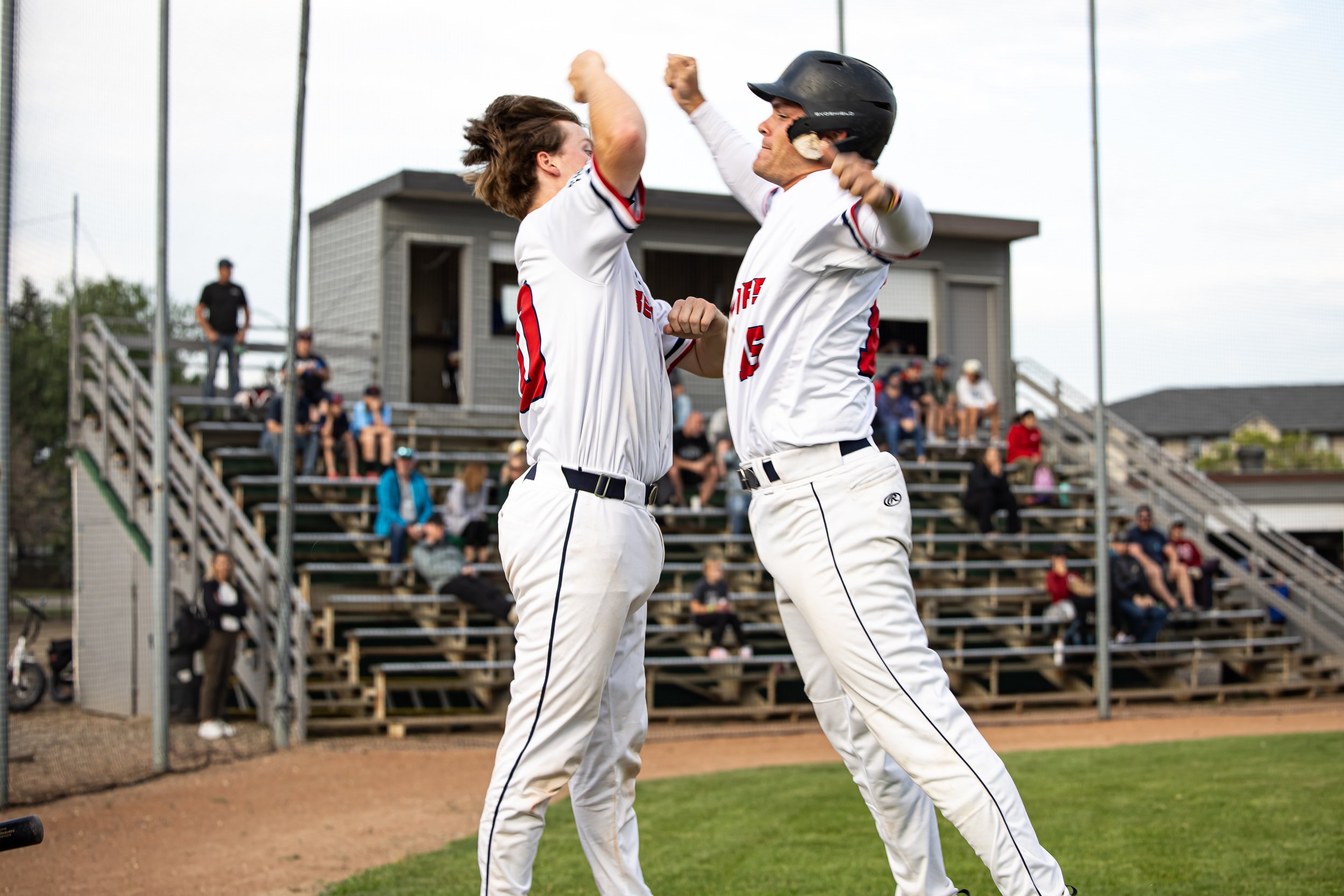 Two baseball players celebrating on the field, with one wearing a helmet and both wearing white uniforms with red and blue accents.