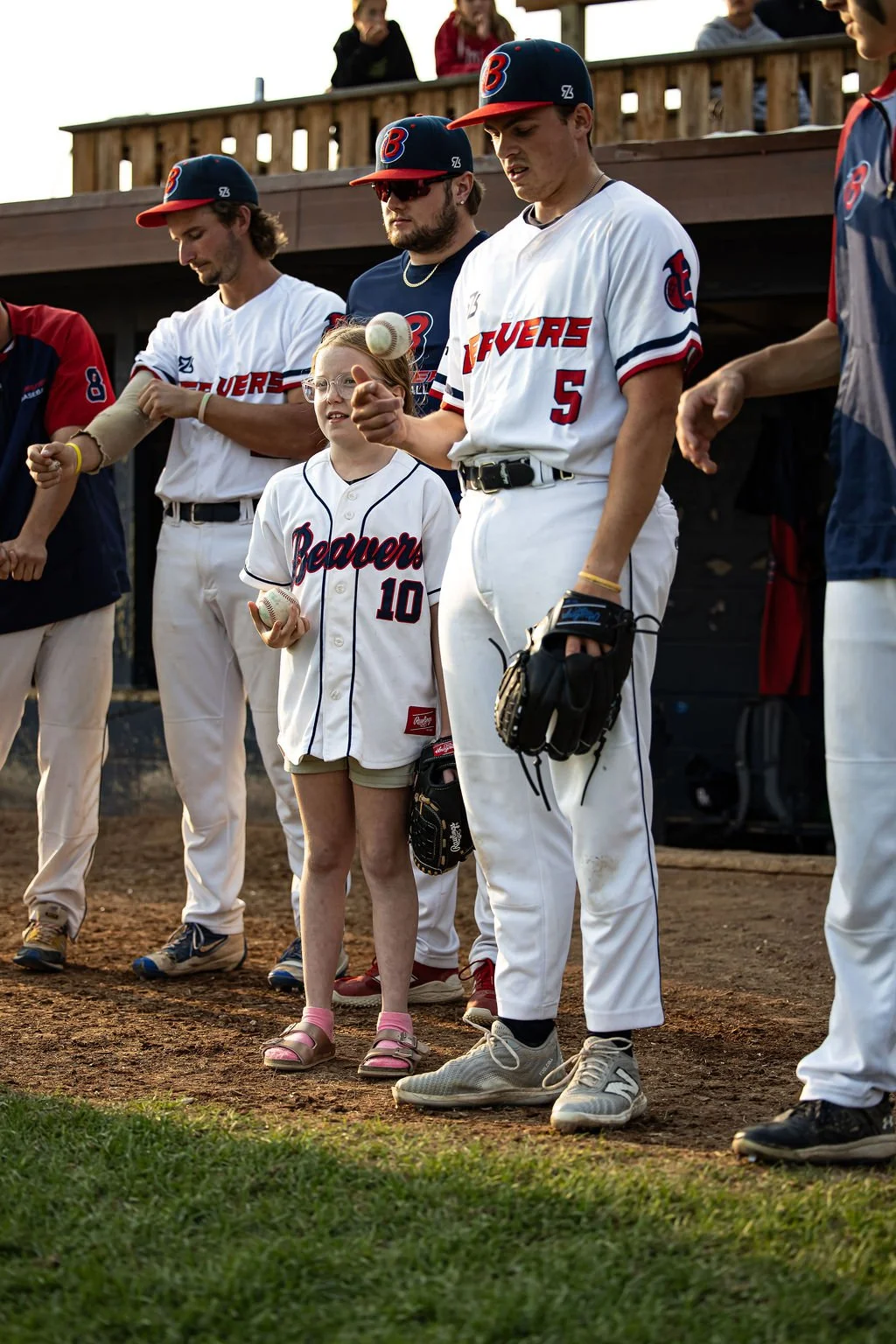 Young girl and baseball players standing on a field during a game or ceremony.