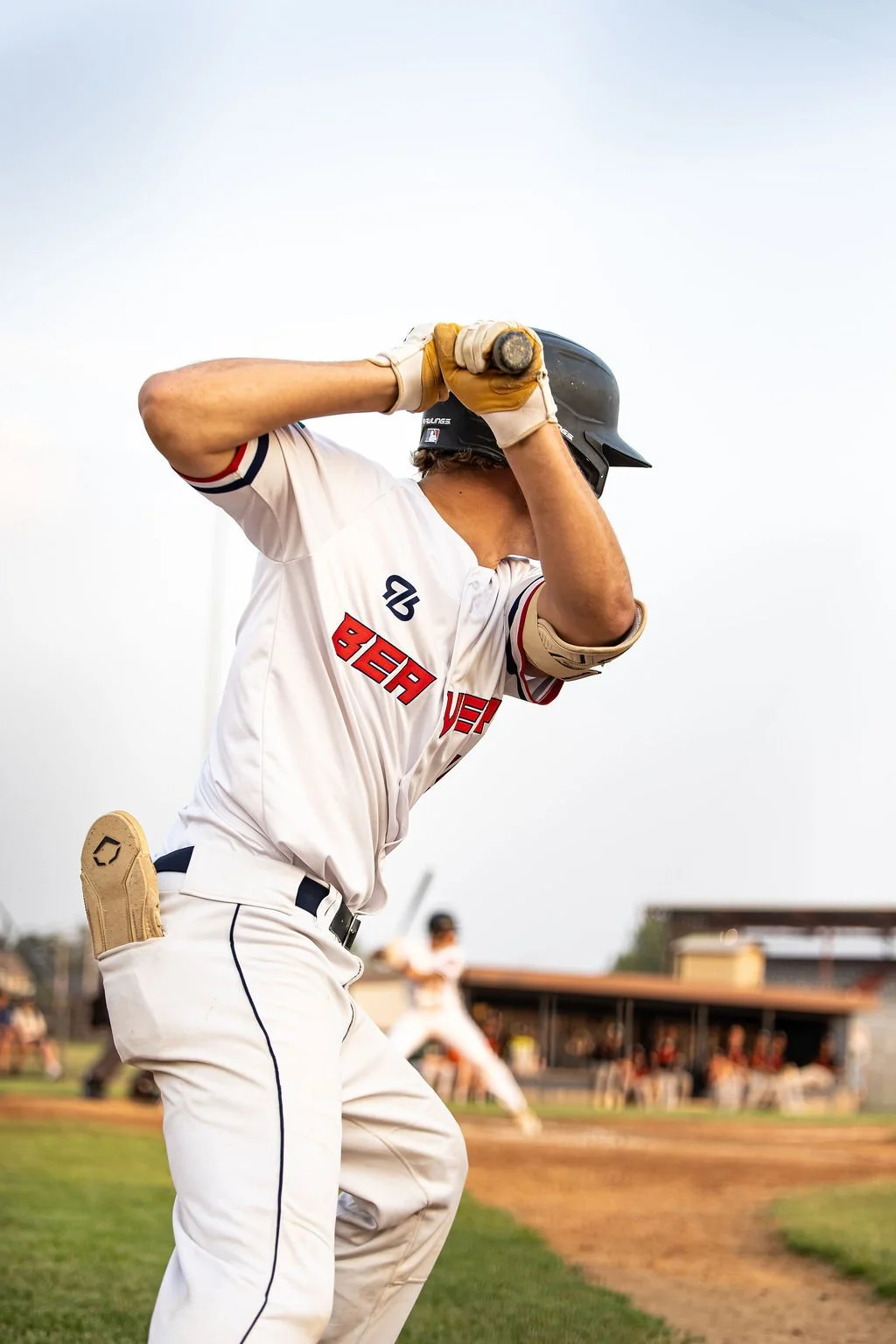 A baseball player in a white uniform with red and black lettering and a black helmet holding a bat at the ready during a game.