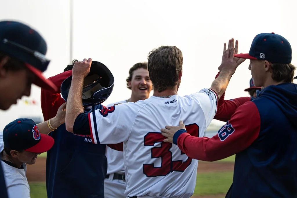 A group of baseball players celebrating on the field, with one player in a white jersey showing the number 32 giving a high-five to a teammate.