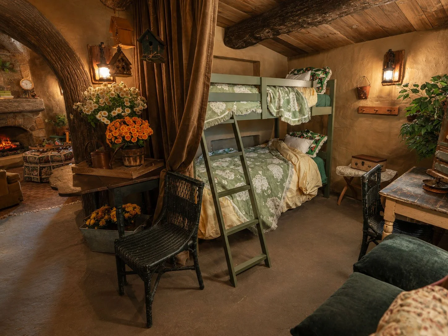 Cozy rustic hobbit-inspired bedroom at Mirador Texas with bunk beds in corner, floral bedding, wooden accents, plants, and a fireplace in the background.