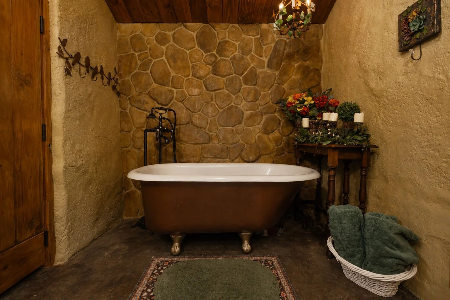 Vintage bathroom with clawfoot bathtub, stone accent wall, wooden door, and floral arrangement on side table.