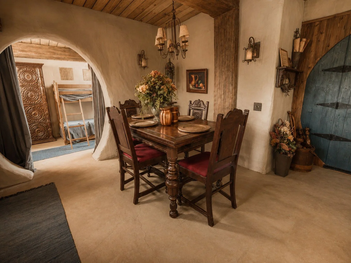 A cozy hobbit dining room at Mirador Texas with a wooden table and four chairs, decorated with a flower arrangement, surrounded by rustic decor and a view into a bedroom with bunk beds.