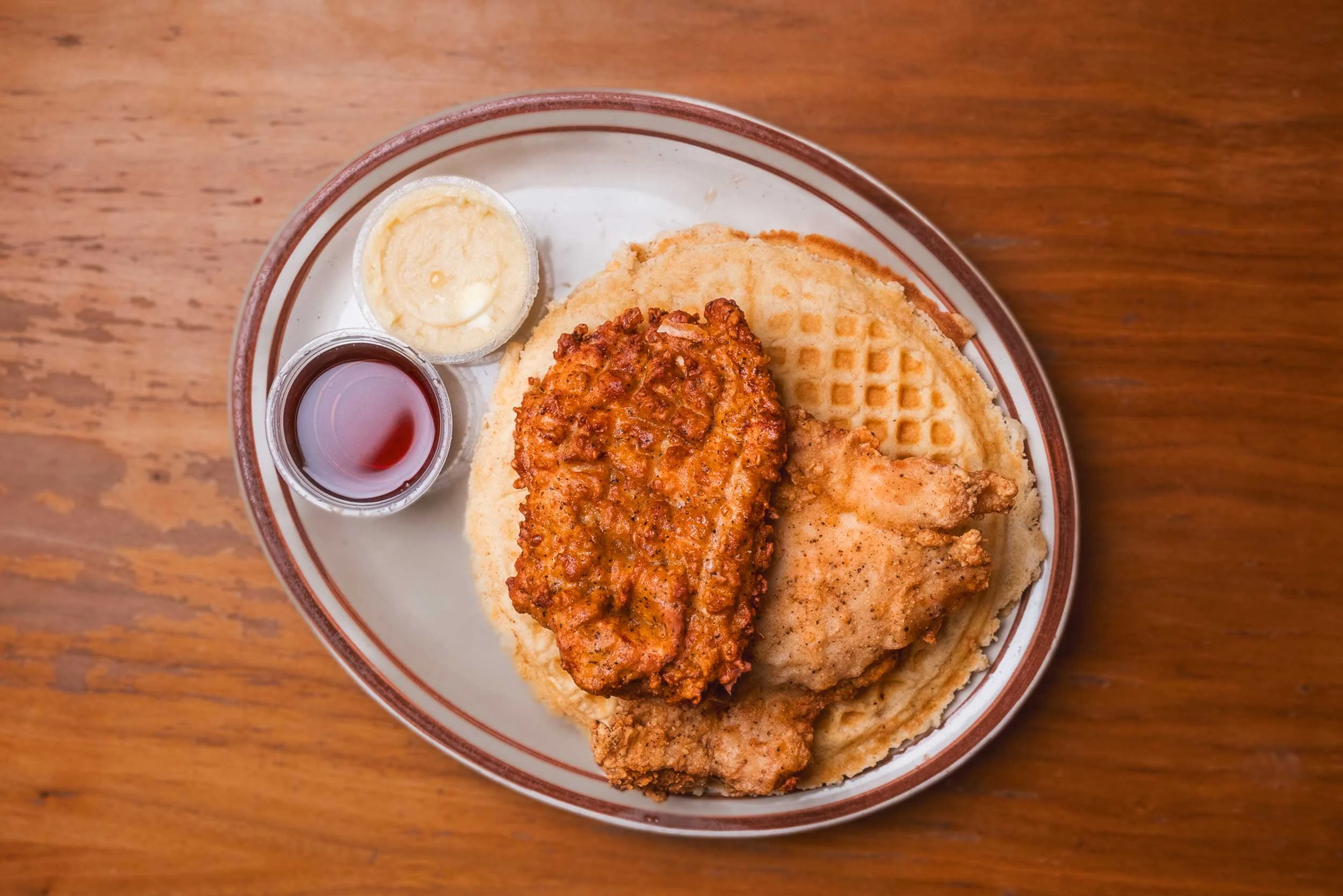 Fried chicken with waffles on a plate, served with syrup and butter.