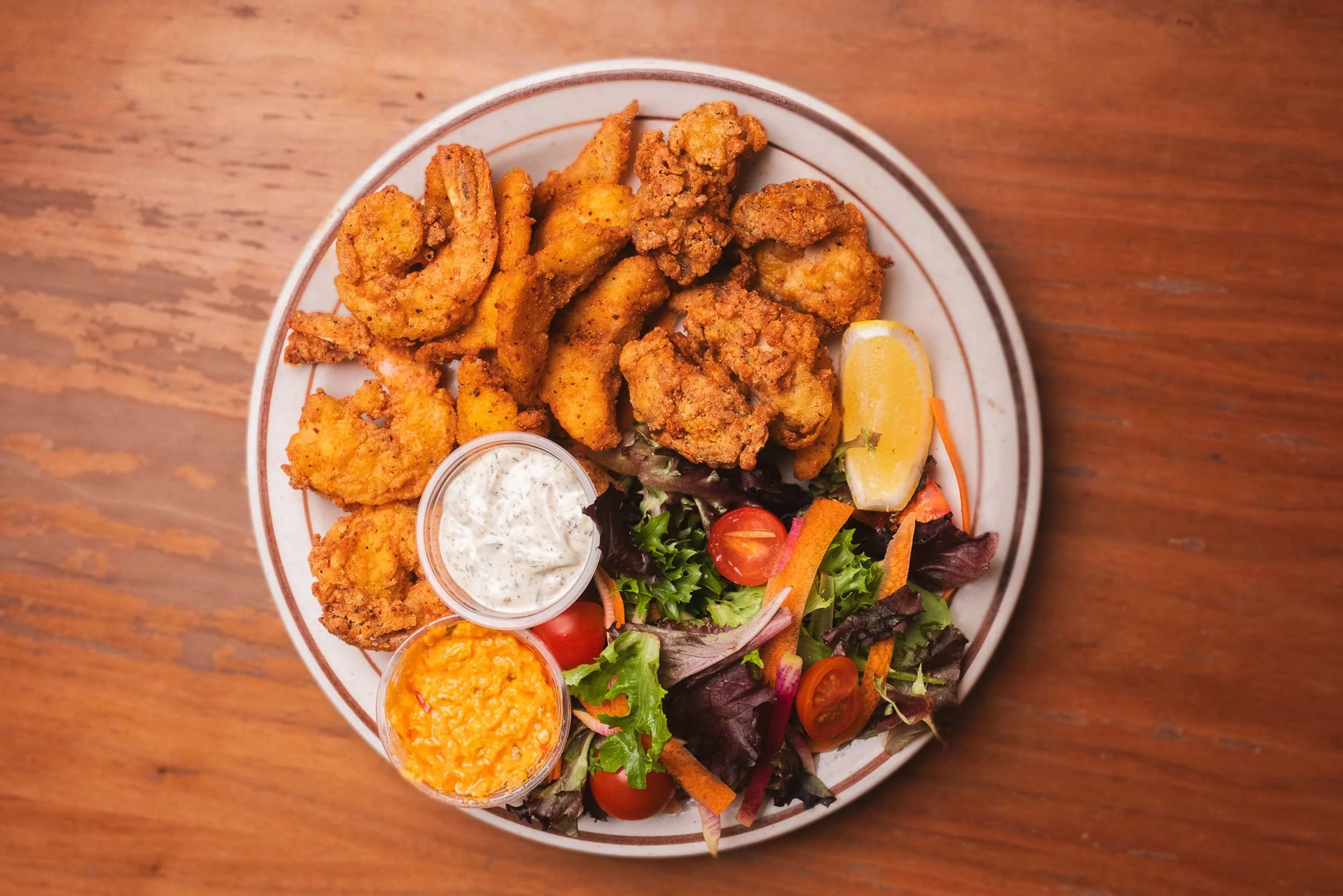 Plate of fried shrimp, fried chicken, salad, and dipping sauces on a wooden table.