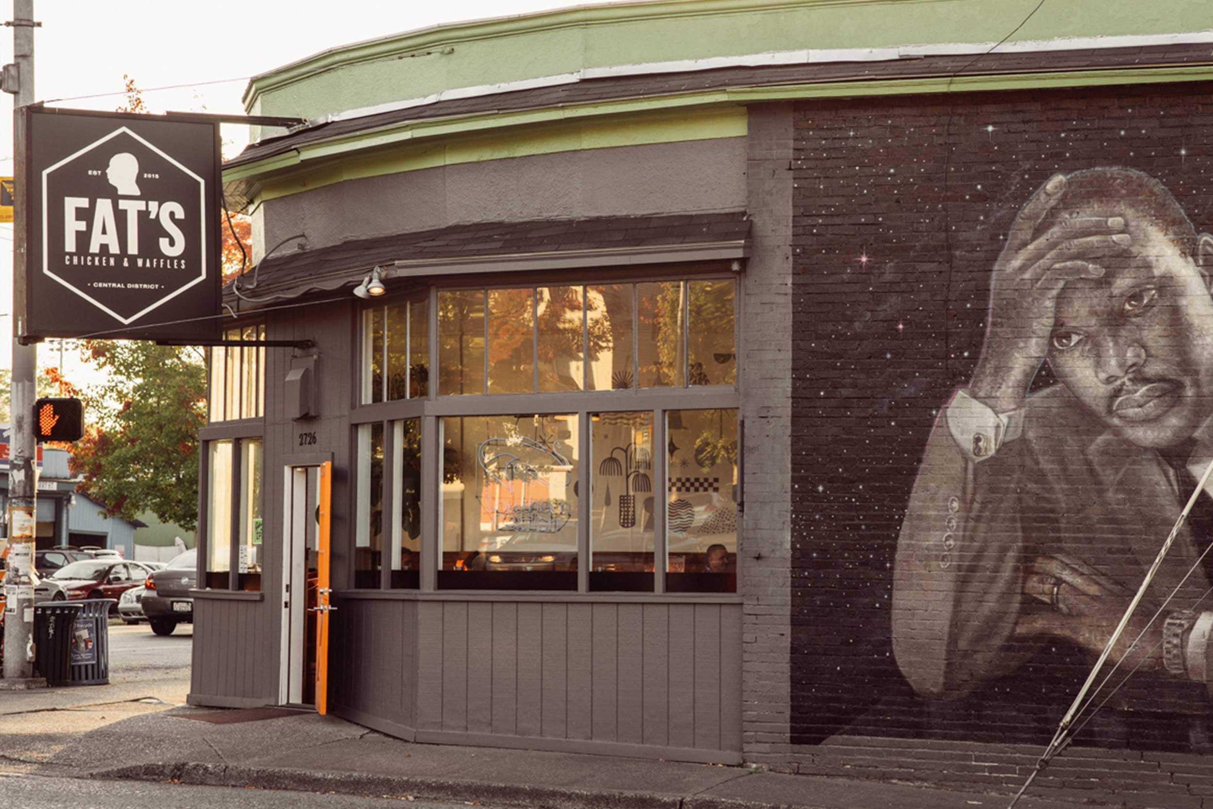 Exterior of a restaurant called Fat's Chicken & Waffles with a mural of a person's face on the brick wall