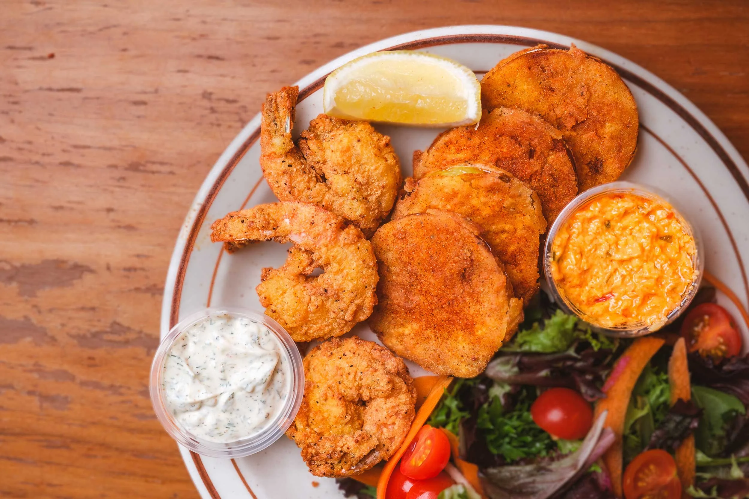 Fried shrimp with lemon wedge, dipping sauces, and fresh salad on a plate.