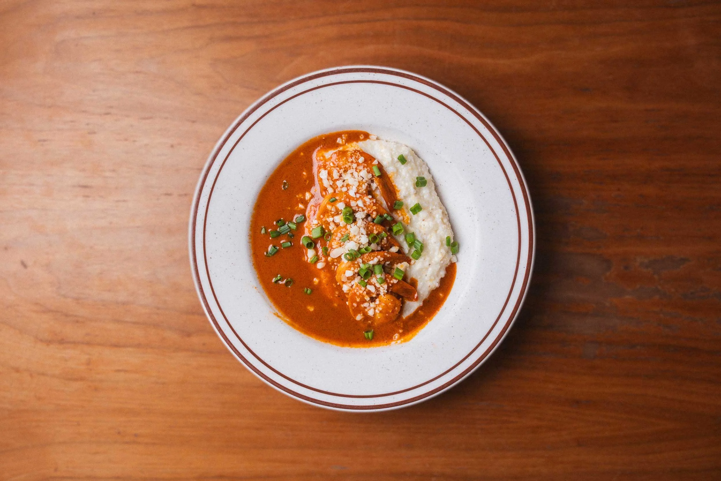 Plate of shrimp and grits, topped with parsley, and grated cheese, placed on a wooden table.
