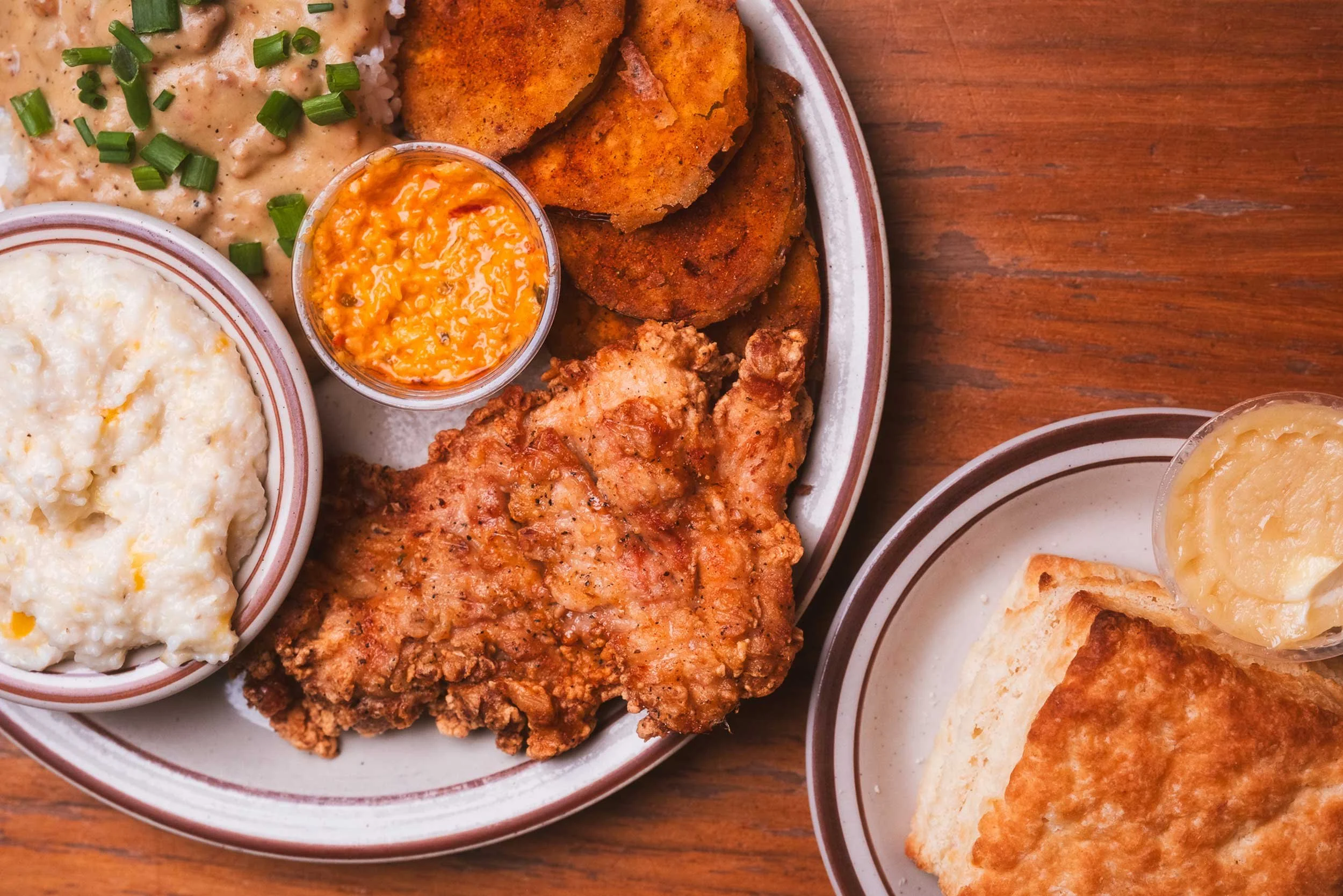 A plate of fried chicken, mashed potatoes with gravy and chopped green onions, cornbread with butter, and fried fish with tartar sauce on the side.