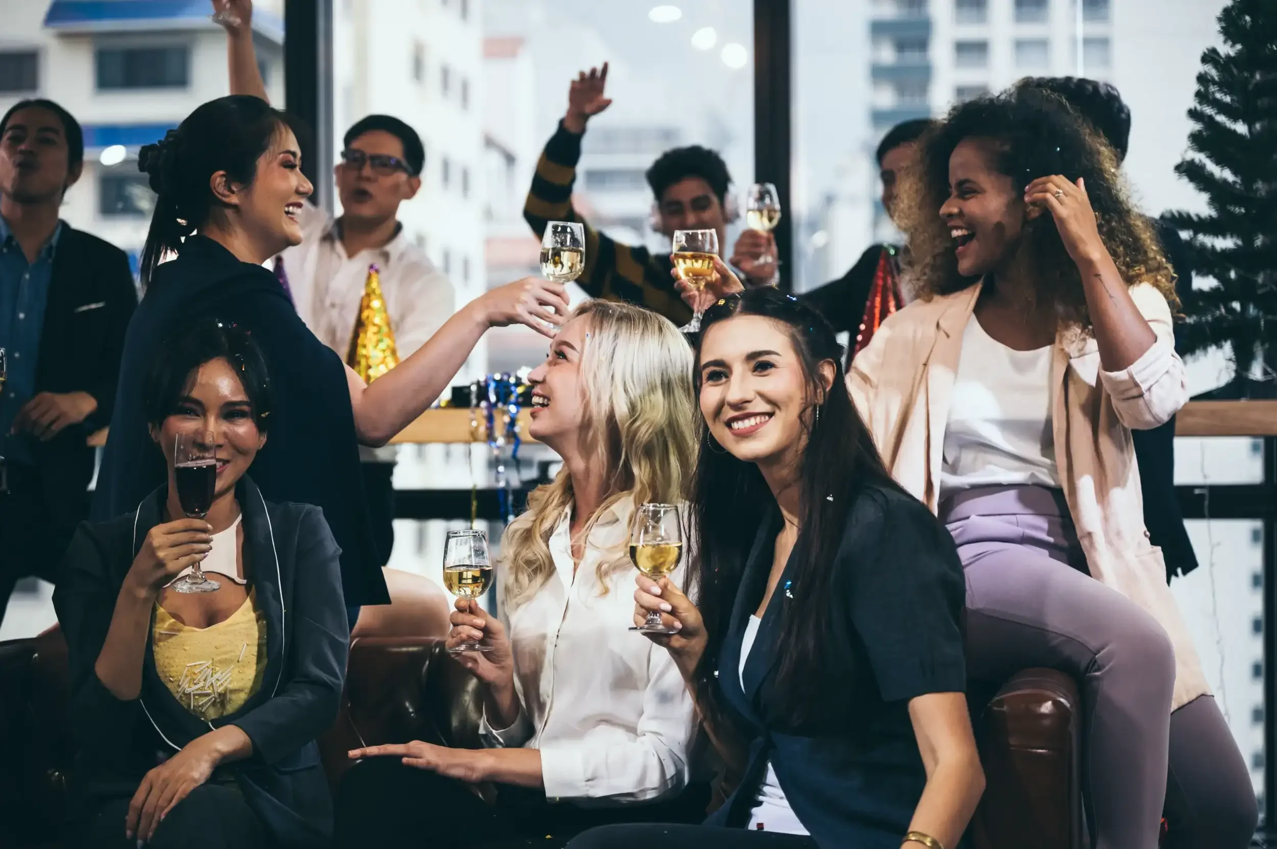 Group of people celebrating with drinks inside a bright, modern space, with some raising glasses of white wine and smiling.