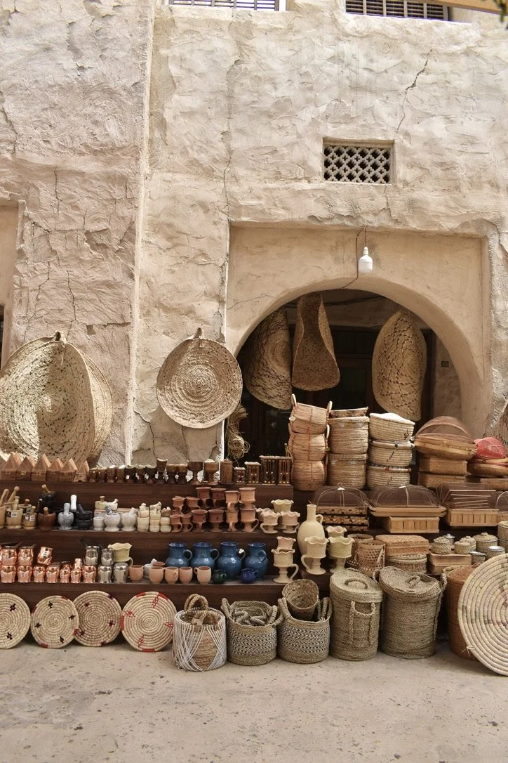 Display of woven baskets, pottery, and wooden items in front of a textured stone wall with an arched entrance.