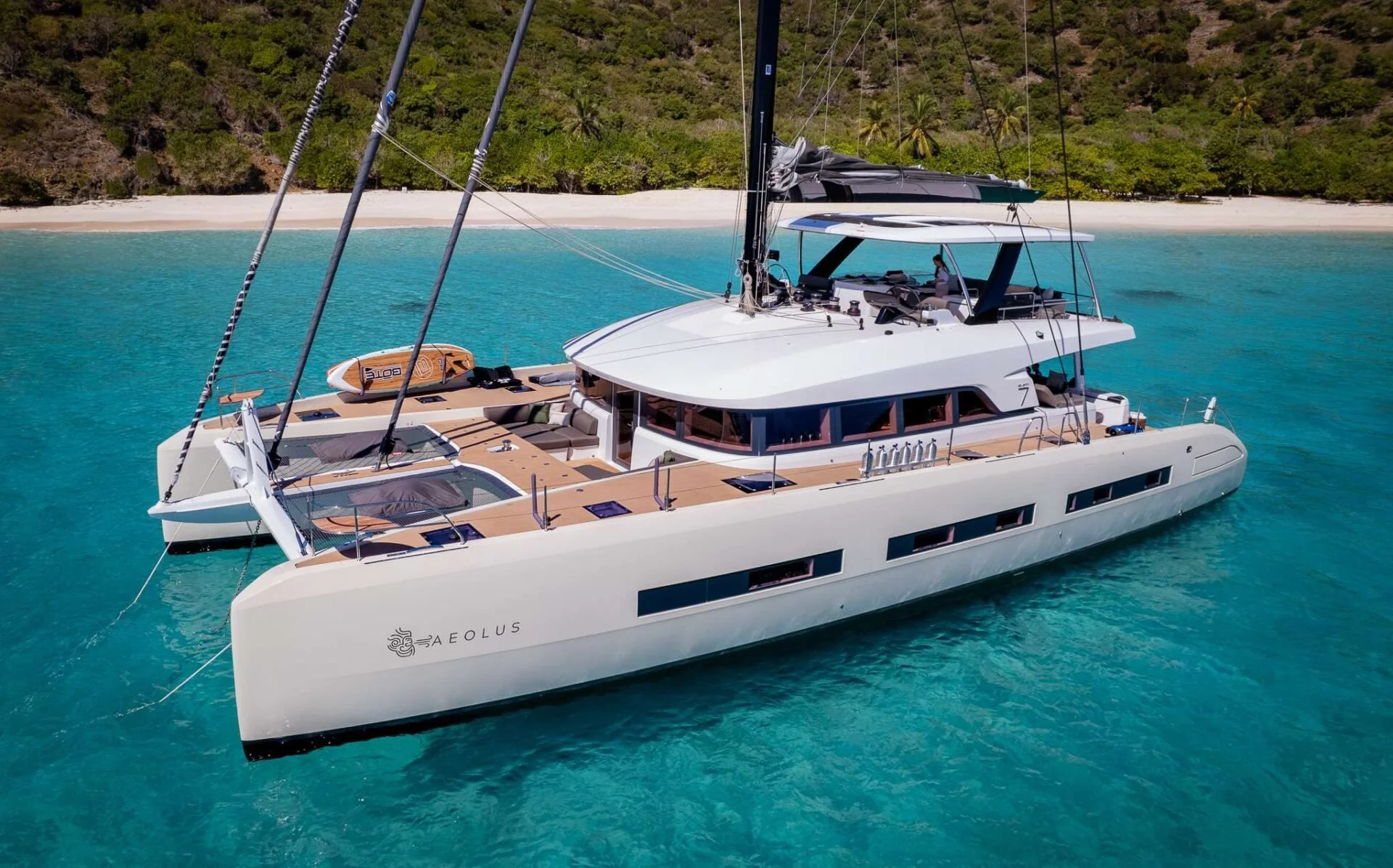 A sleek white luxury yacht named AEOLUS floating on turquoise water with a green, tropical island beach and trees in the background.