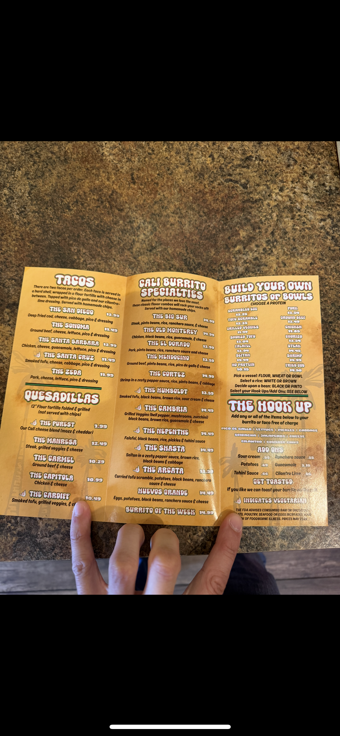 A person holding a Mexican restaurant menu on a brown textured table.