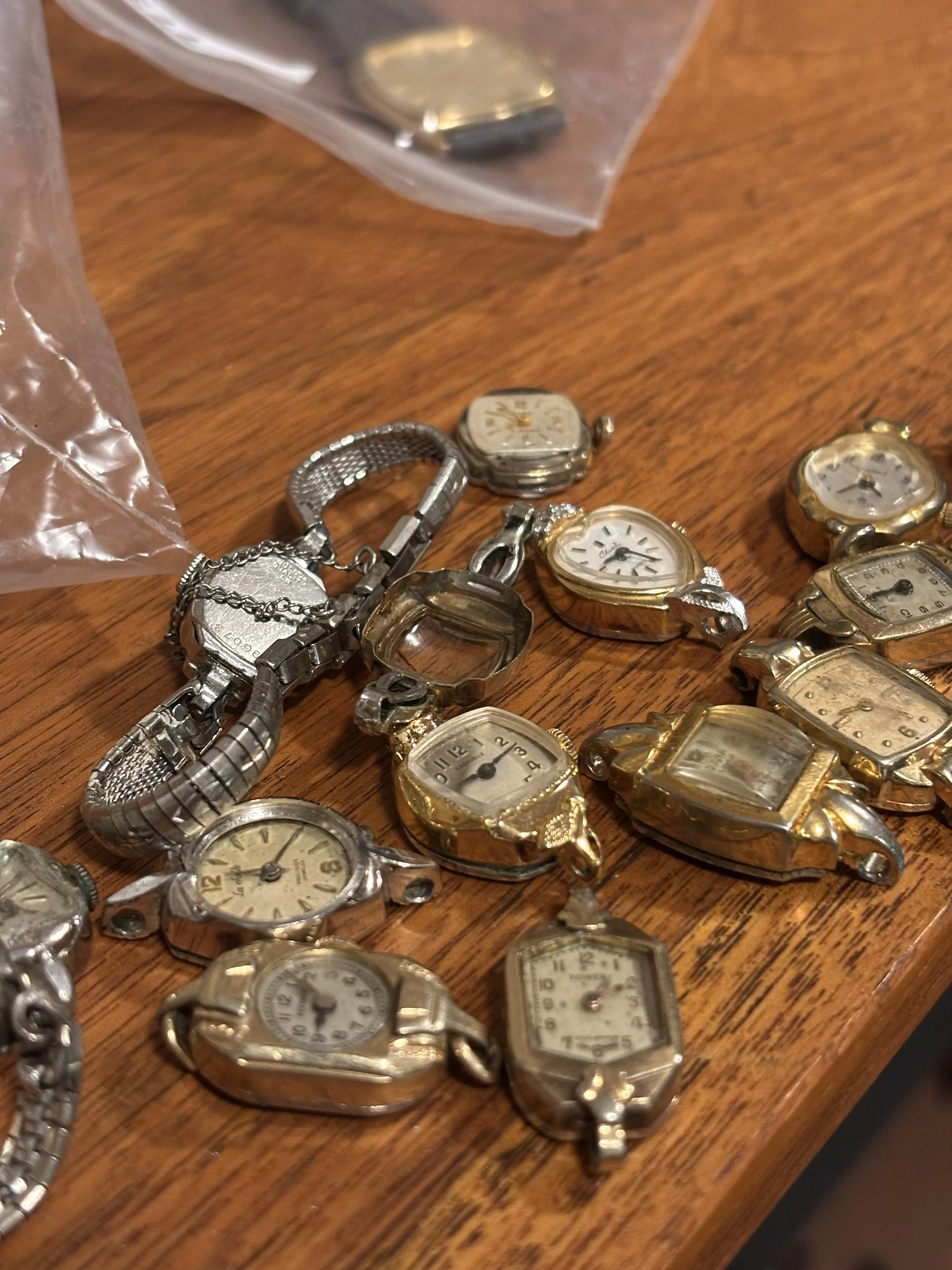 Collection of vintage wristwatches with metal bands laid out on a wooden surface, some in a plastic bag.