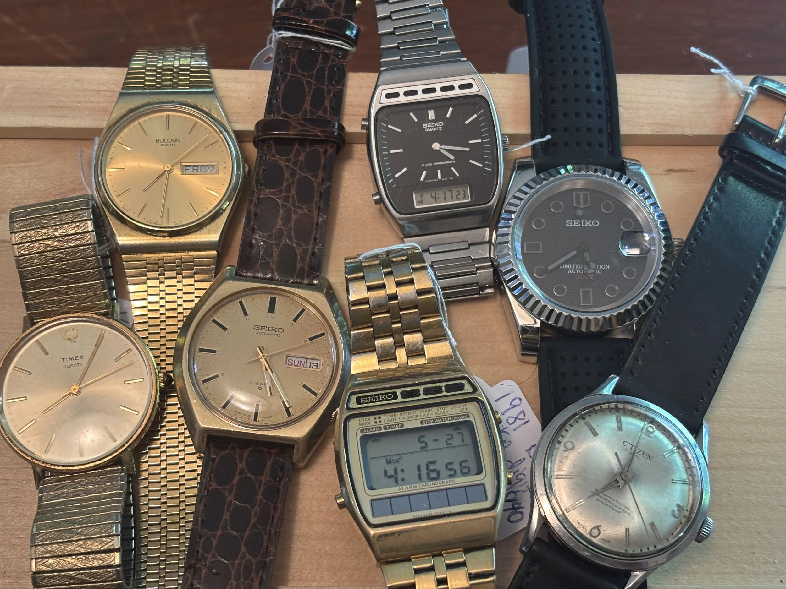 Collection of various wristwatches with different designs and bands, displayed on a wooden surface.