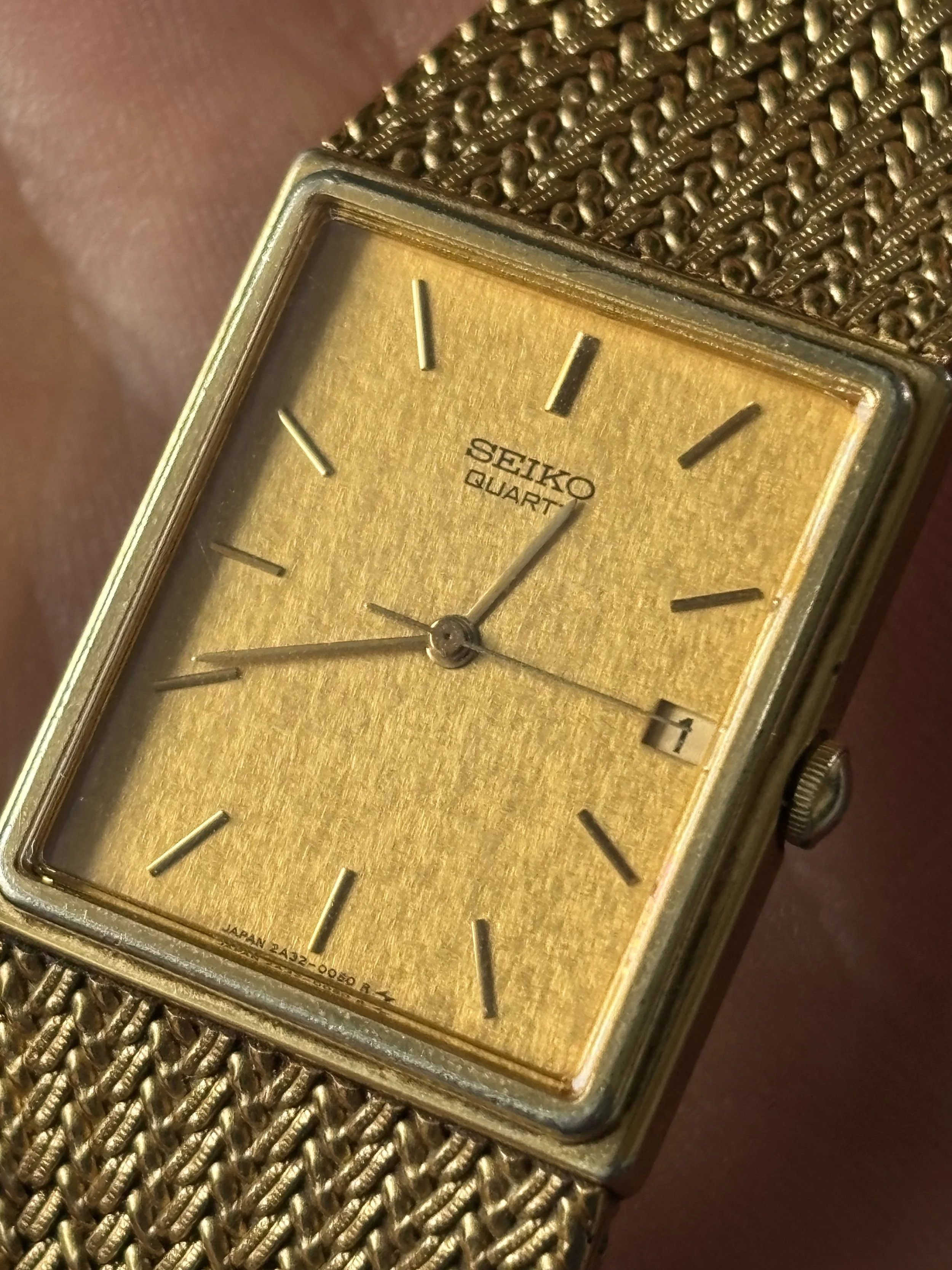Close-up of a vintage gold-toned Seiko quartz wristwatch with a metallic mesh band and gold-colored dial.