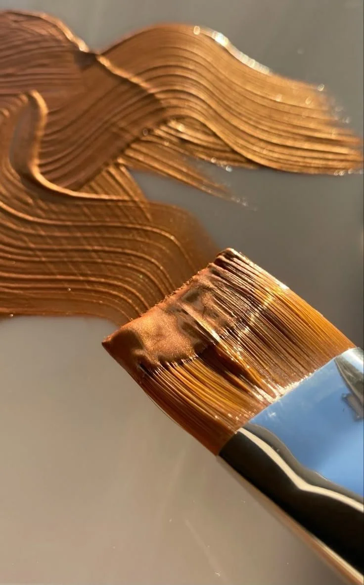 Close-up of a paintbrush with copper-colored paint reflecting light.