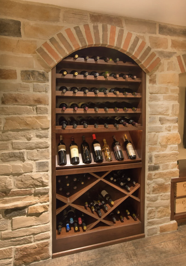 Wooden wine rack built into a brick wall, holding multiple bottles of wine on shelves and in diamond-shaped compartments.
