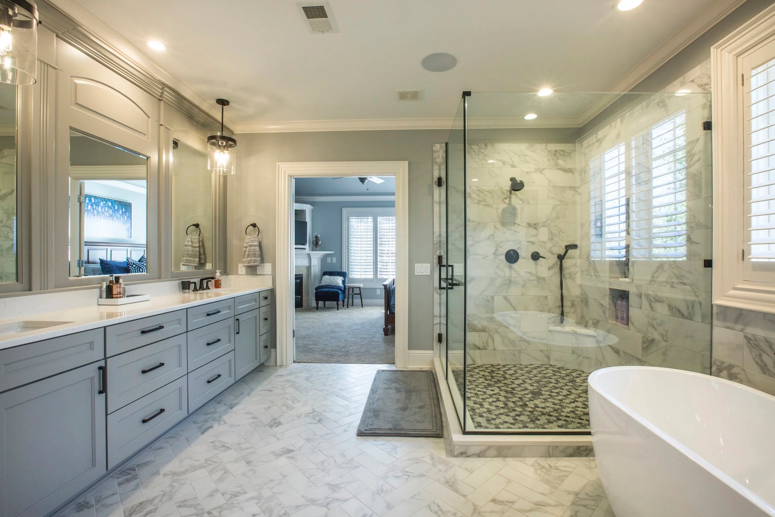 Modern bathroom with large vanity mirror, white cabinetry, marble floors, and a walk-in shower with glass door and marble tiles, next to a bathtub.