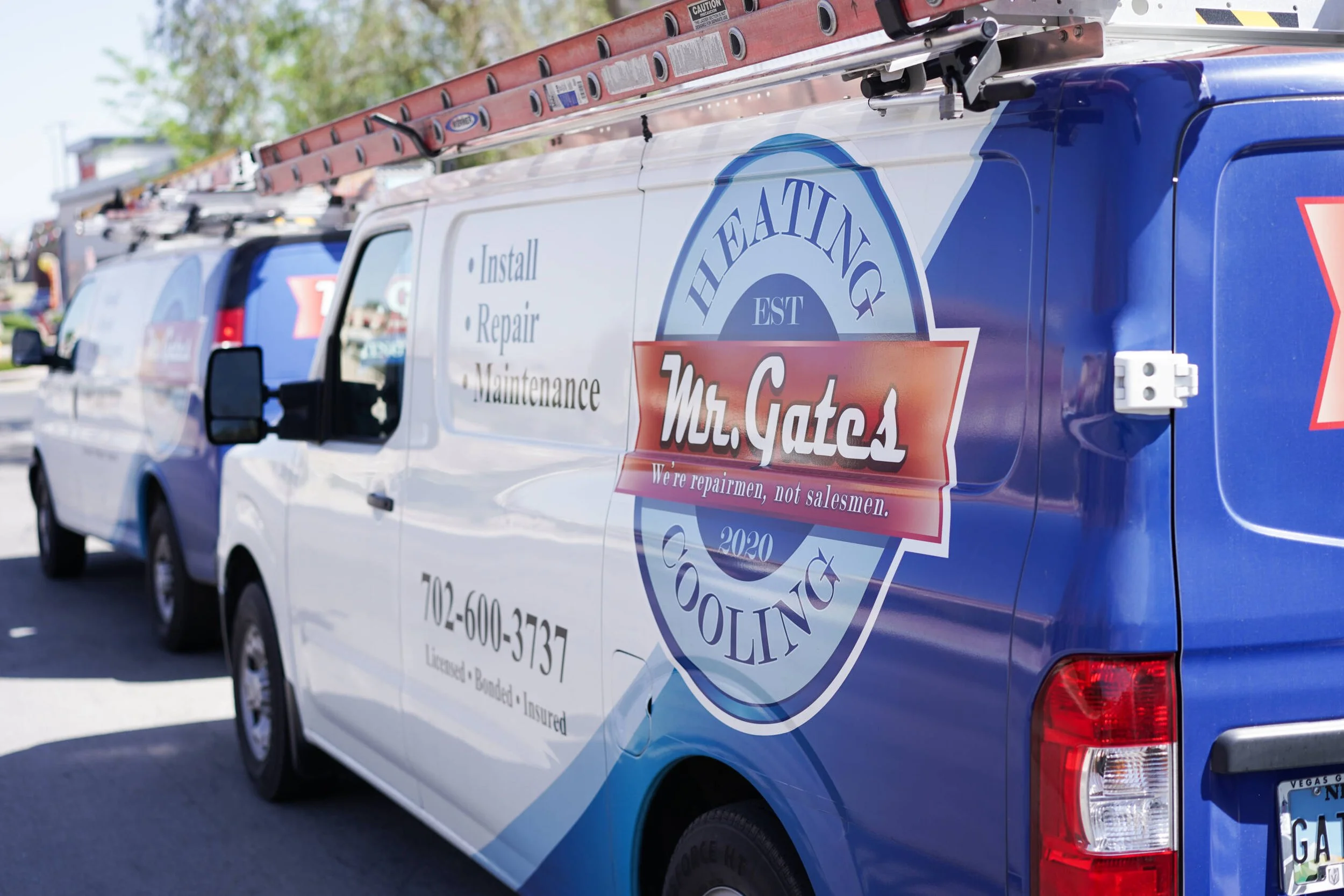 Side view of a white service van with blue accents, displaying logo and contact information for Mr. Gatos in Las Vegas, Nevada. The van is equipped with a ladder on top, suggesting it is used for repair, installation, or maintenance services.