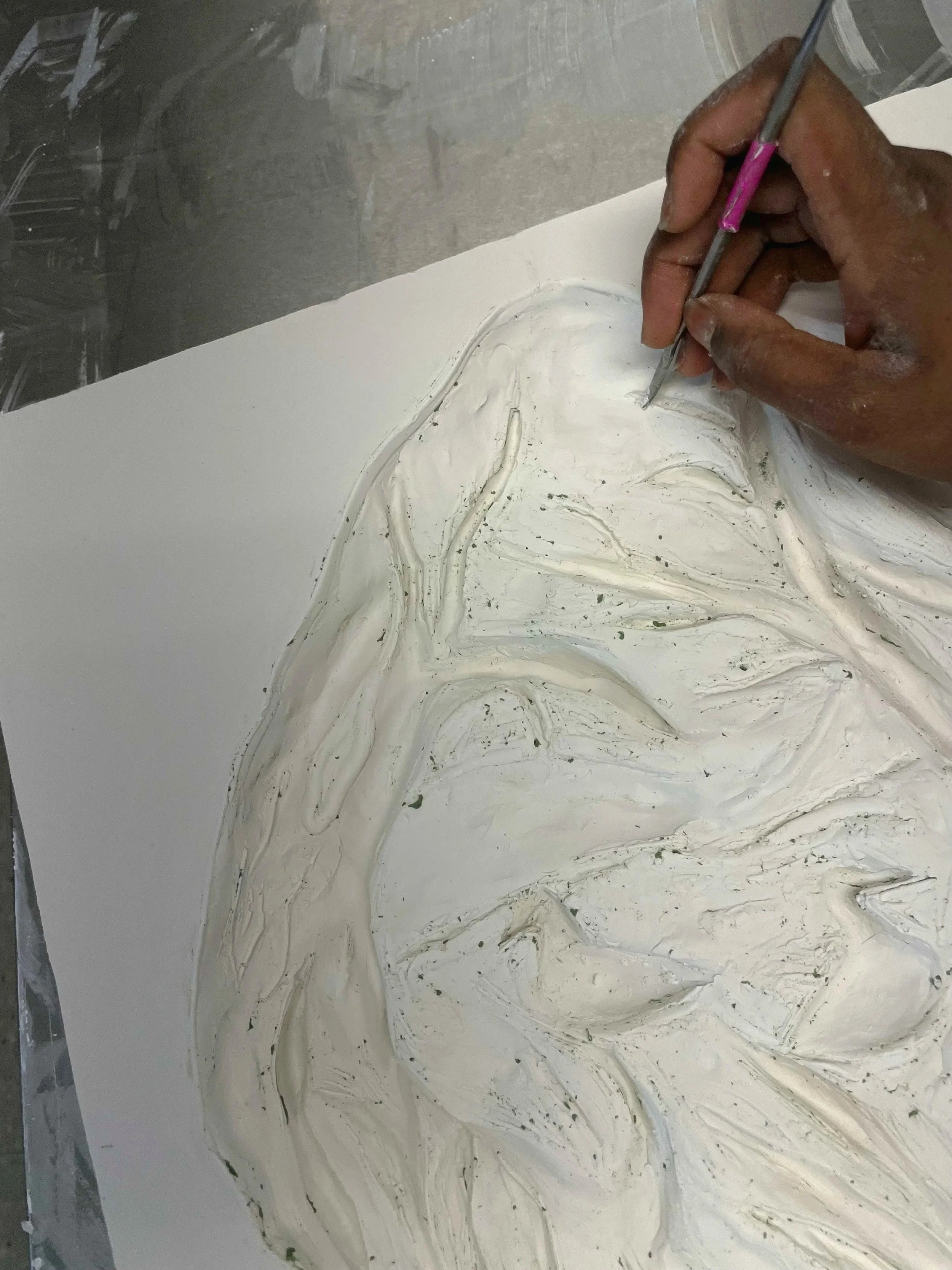A person's hand  is carving a design into a white surface with a small tool, with swirls and textured patterns in the material.