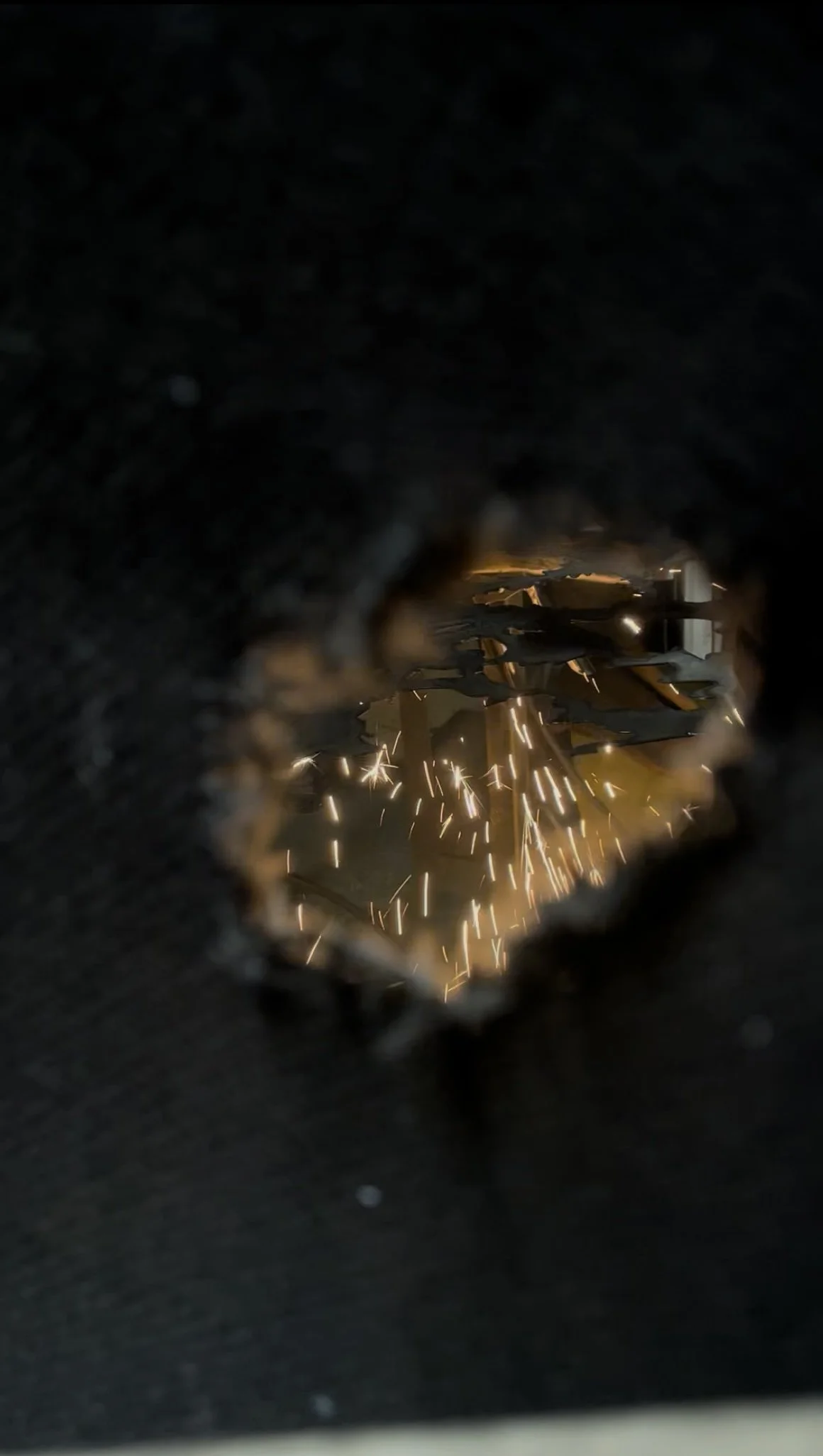 Welding sparks flying from a welding machine, viewed through a small opening.