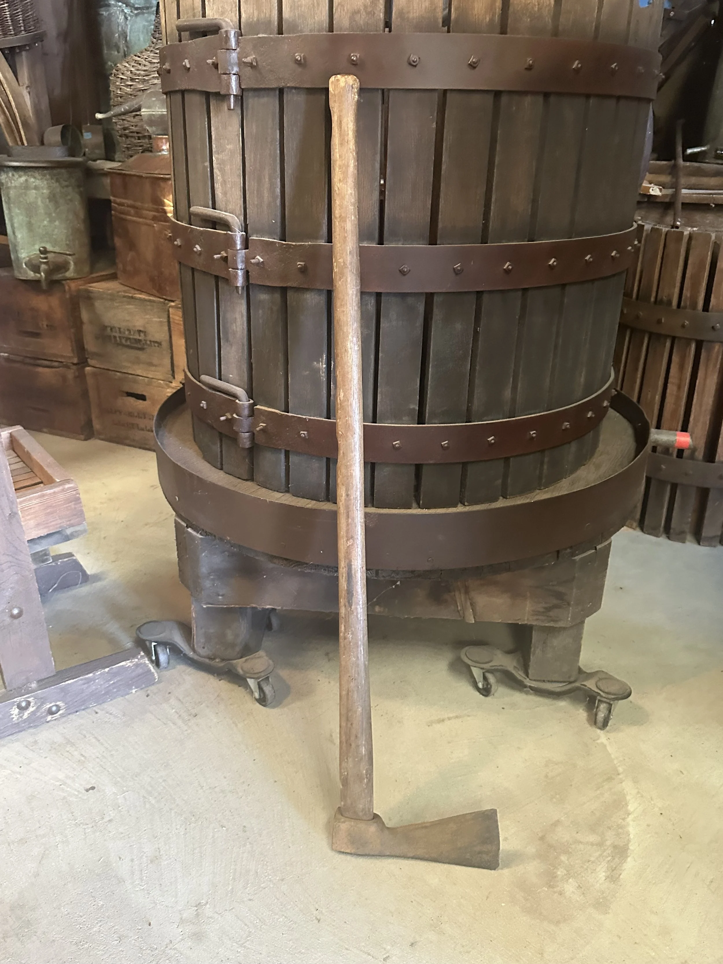 A long handled axe resting against a grape press.