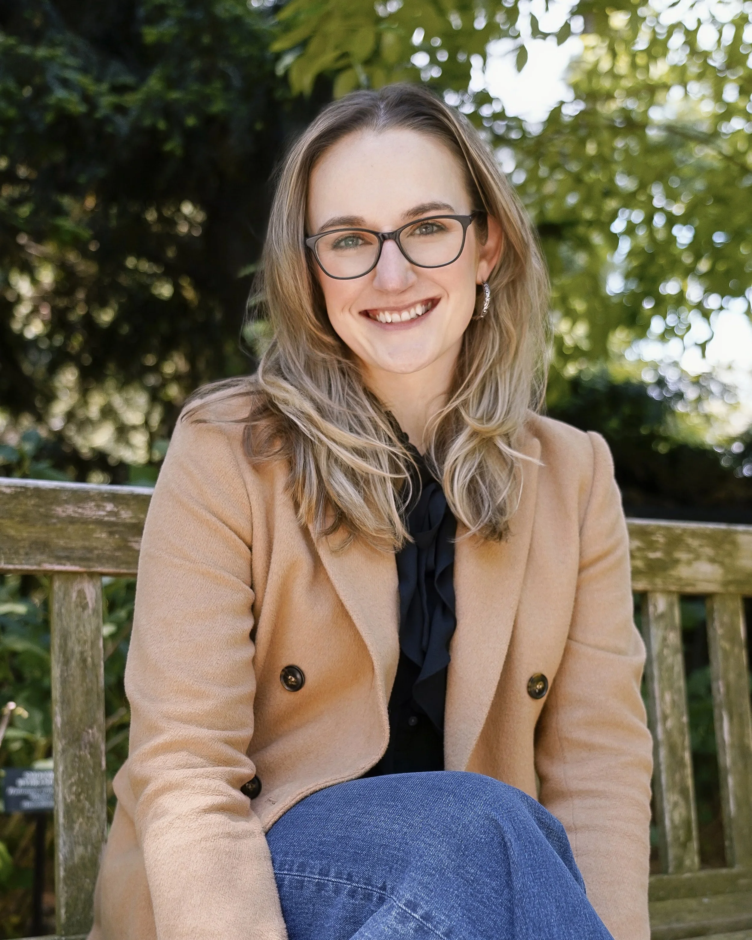 A headshot of Dr. Carly Doucette sitting on a bench in the woods