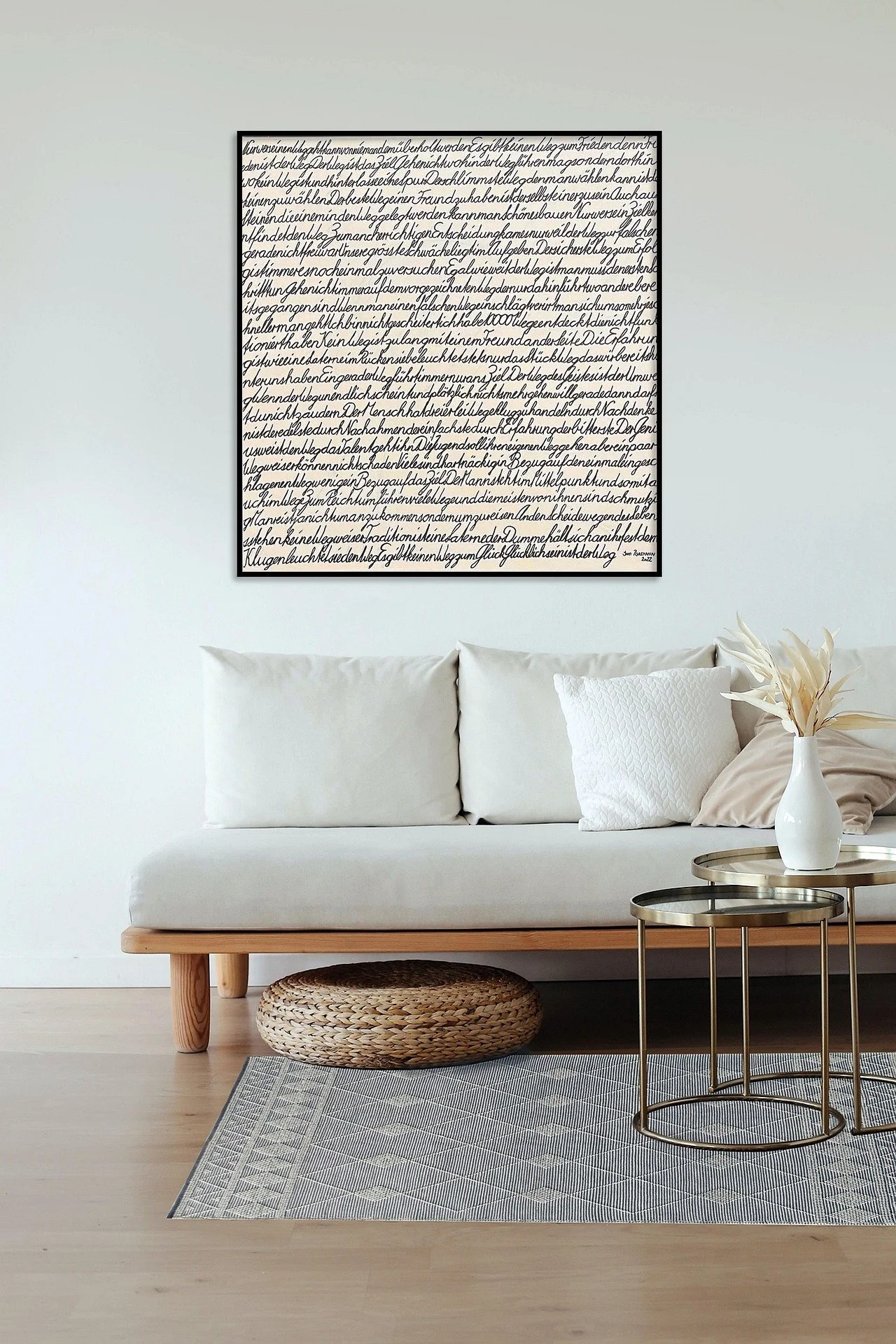 A minimalist living room with a white sofa, decorative pillows, a black and white abstract artwork on the wall, a woven basket, a round side table, and a vase with white flowers.