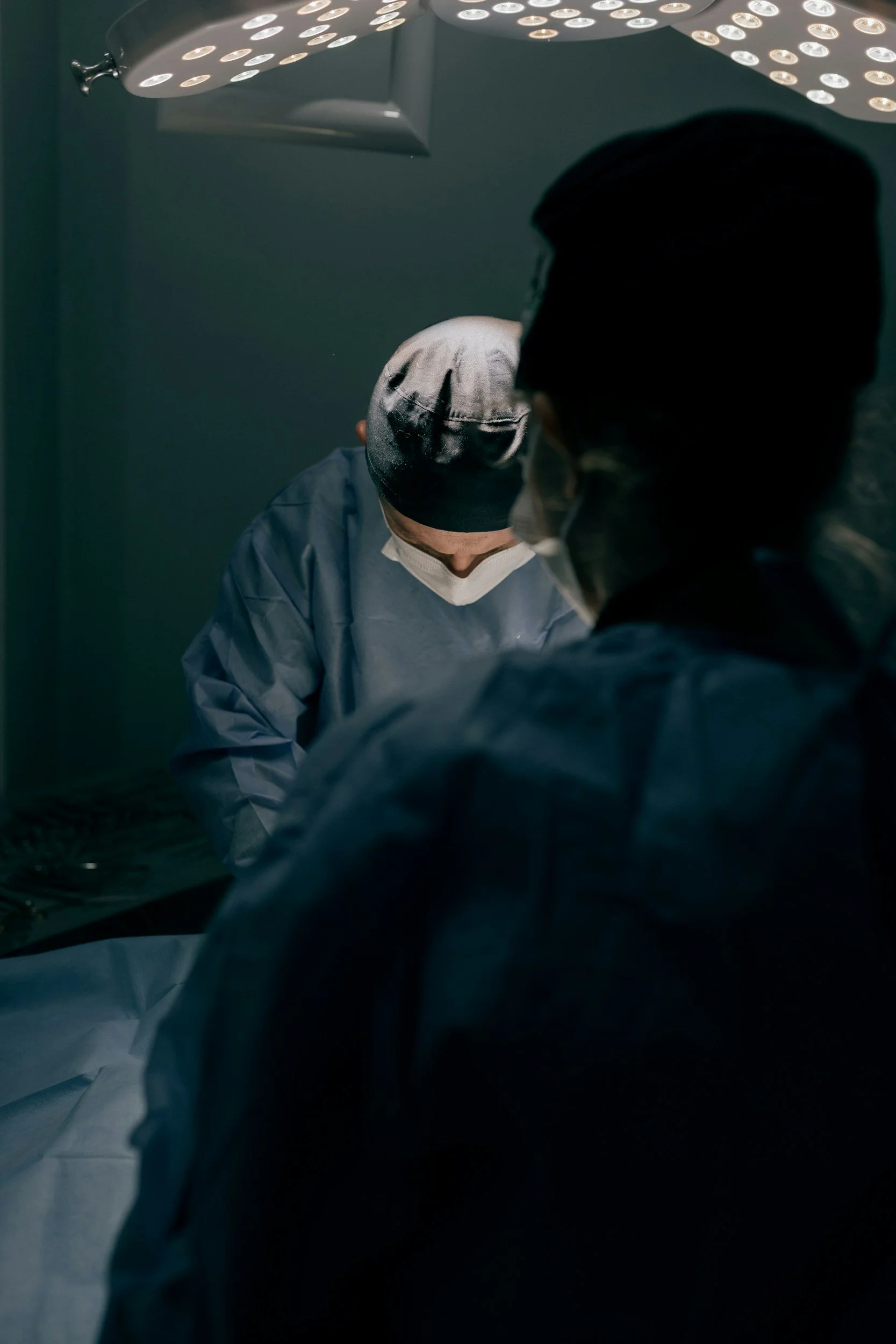 Medical professionals performing surgery in an operating room, focusing on their heads and upper bodies with surgical masks and caps.
