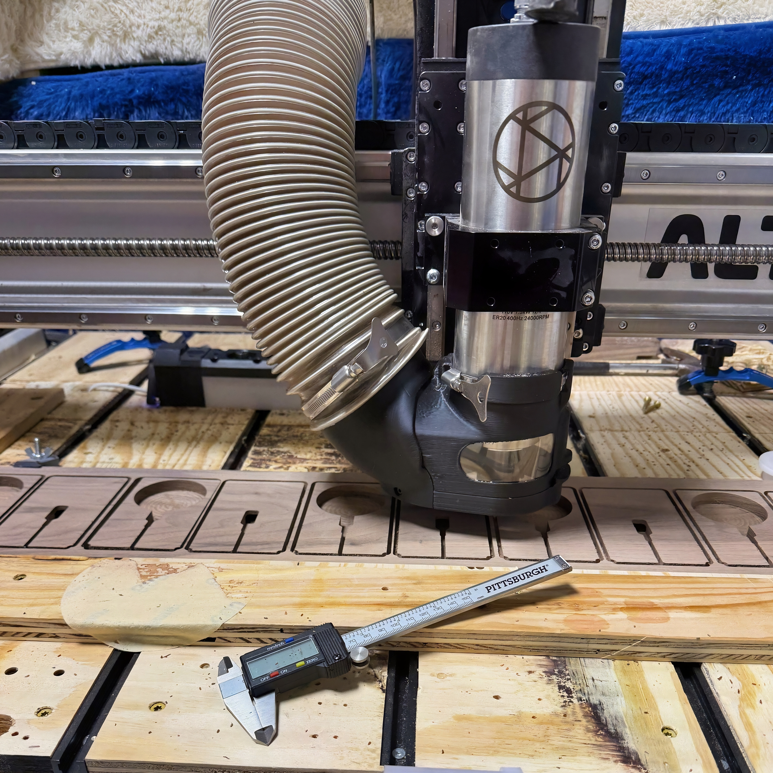 Close-up of a CNC machine tool with a flexible hose and metal components, on a wooden work surface with measuring tools.