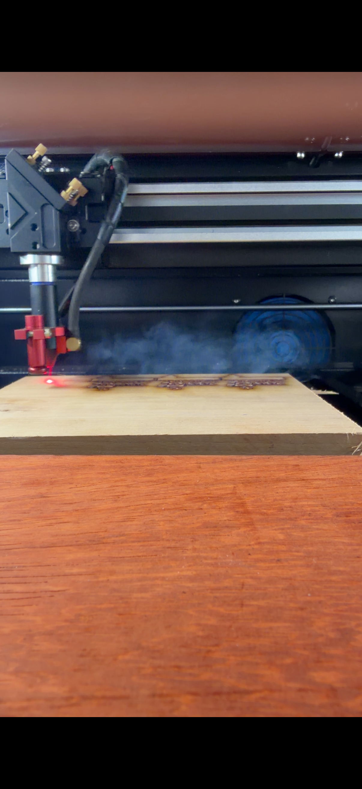 A laser engraver machine is carving designs into a wooden piece.