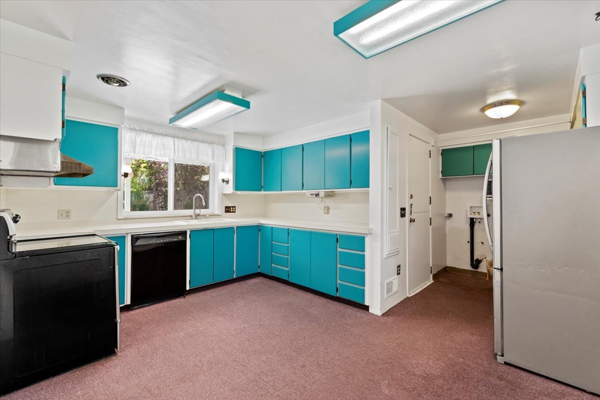 Kitchen with blue cabinets, white countertops, black appliances, and a window above the sink.