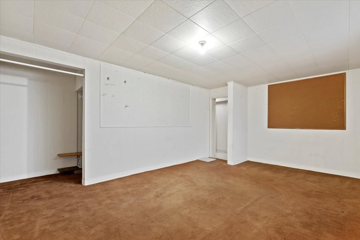 Empty room with white walls, brown carpet, and two corkboards on the walls, one on the right and one on the left.