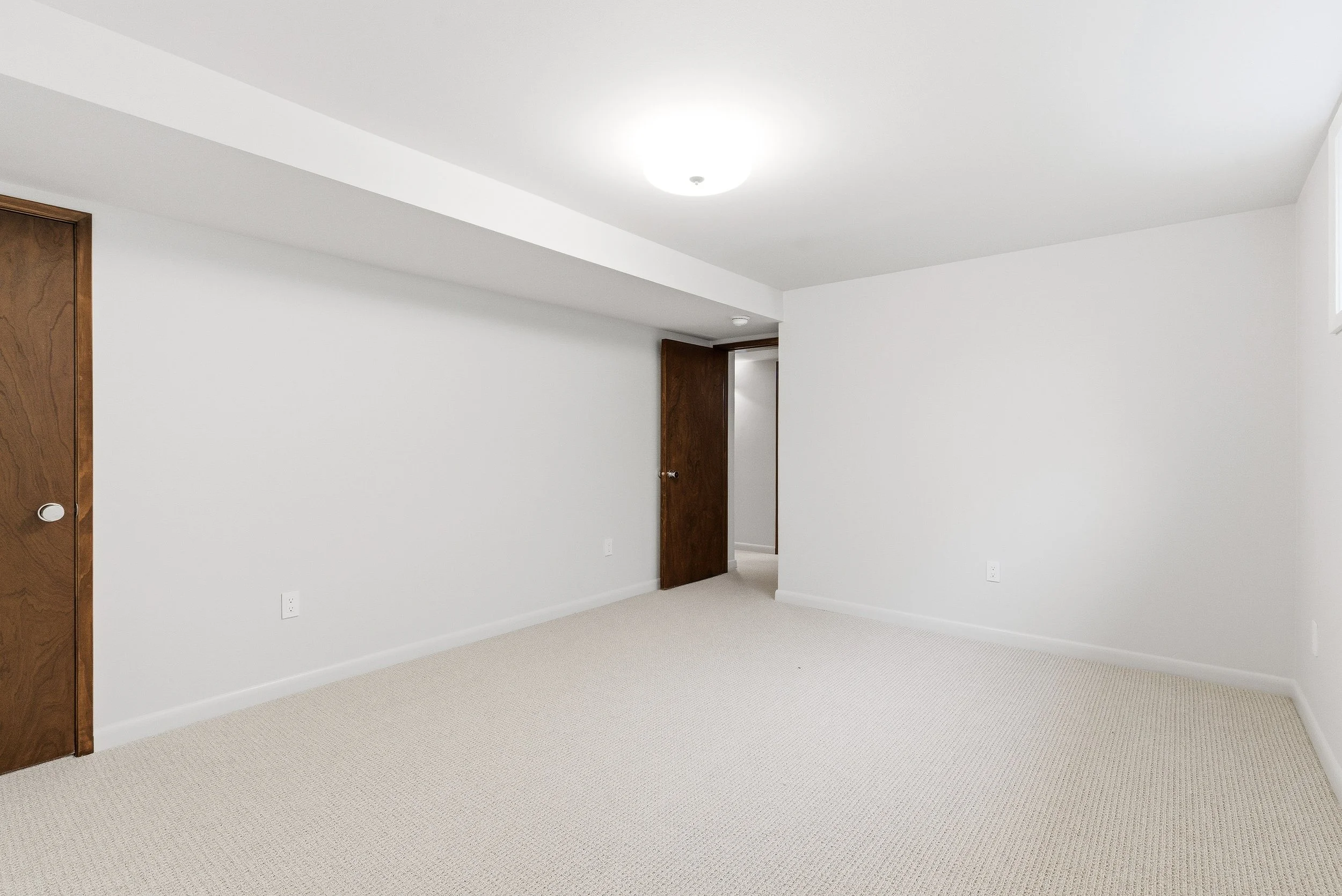 Empty room with white walls, beige carpet, dark wood doors, and ceiling light.