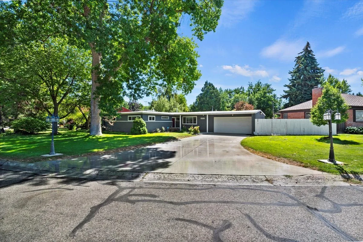 Single-story house with gray exterior, attached garage, surrounded by green lawn and trees, on a sunny day with blue sky.