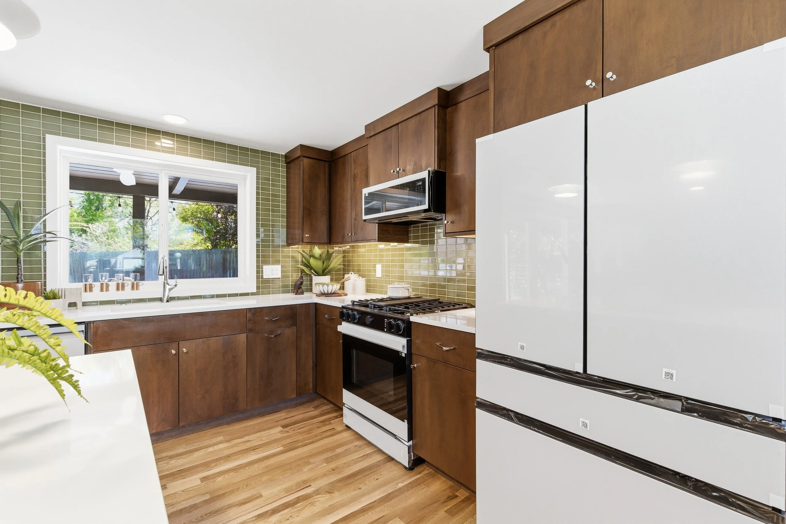 Kitchen with wooden cabinets, a stove, a microwave, a window, green tile backsplash, a white refrigerator, and wood flooring.