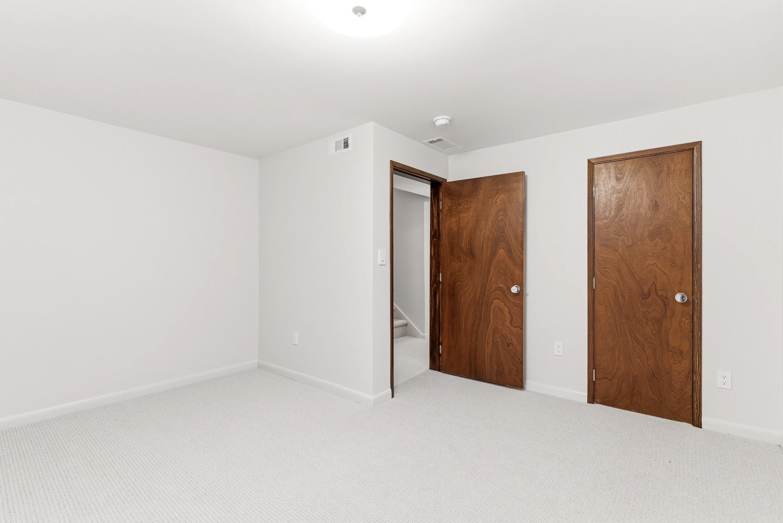Empty white room with two wooden doors and beige carpet.
