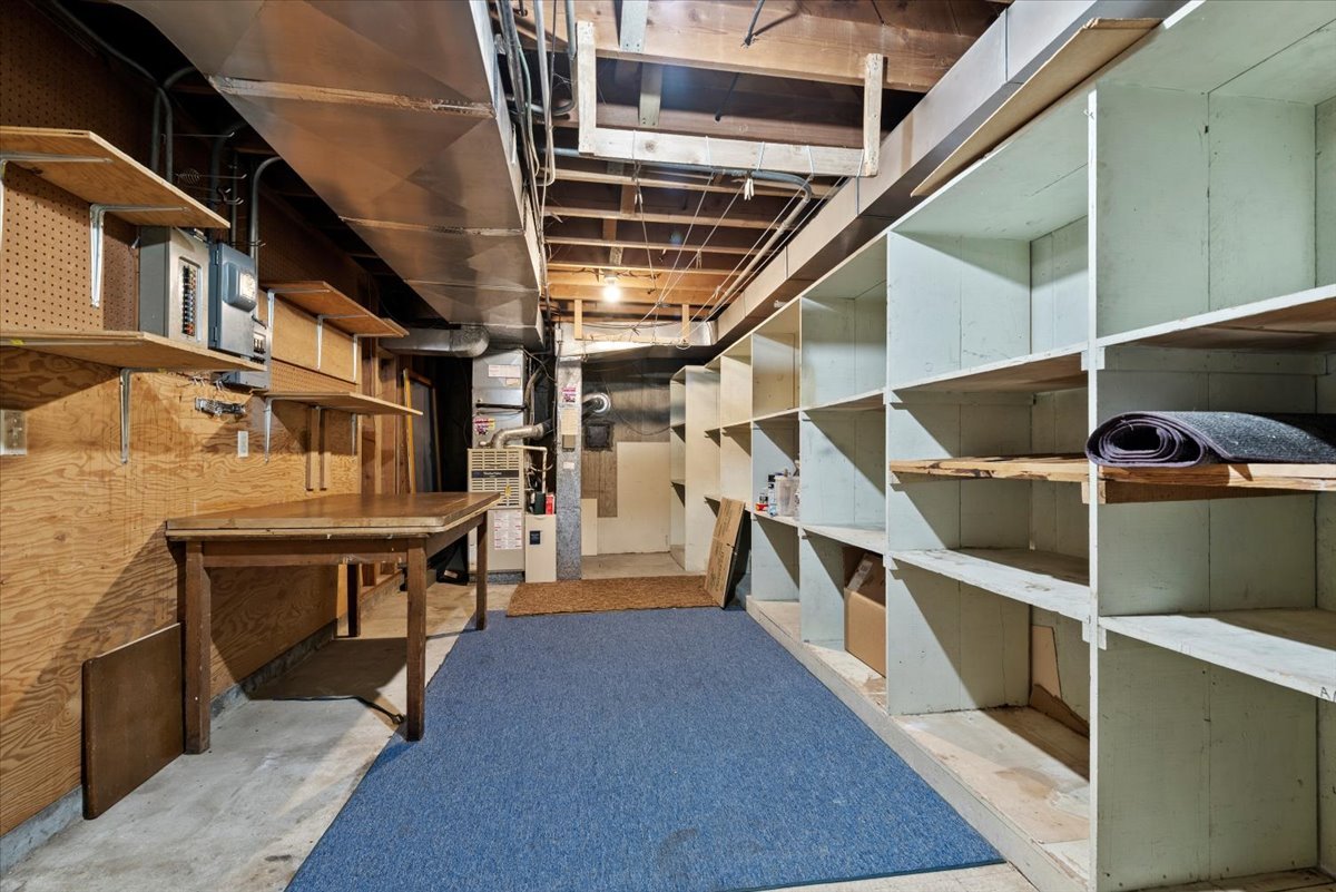 Empty basement storage room with wooden shelves, a workbench, and a blue rug on the concrete floor.