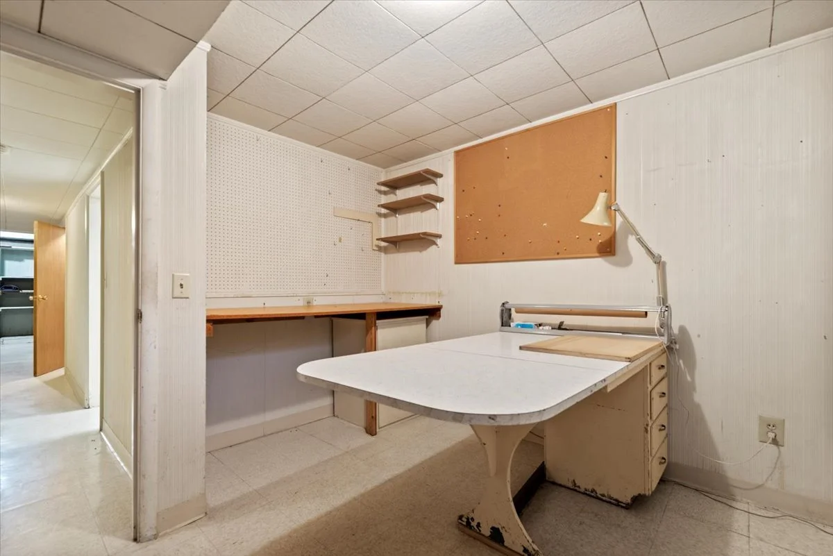 Empty room with a drafting table, cork and pegboard walls, and wall-mounted shelves.