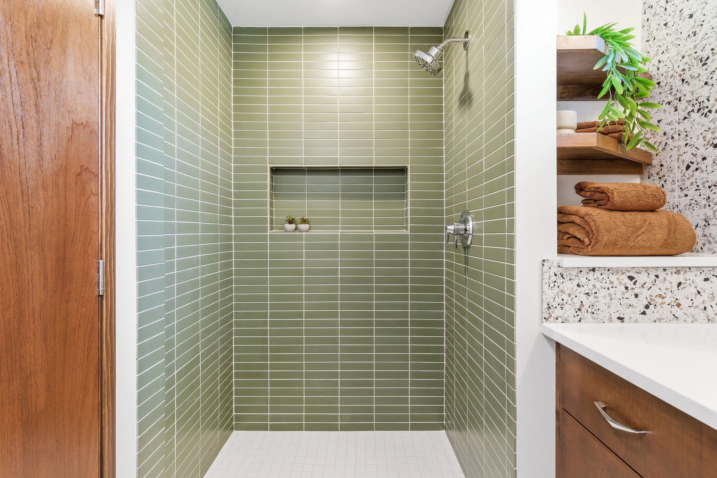 Modern shower with green tile walls, small built-in shelf with two small potted succulents, and a showerhead.