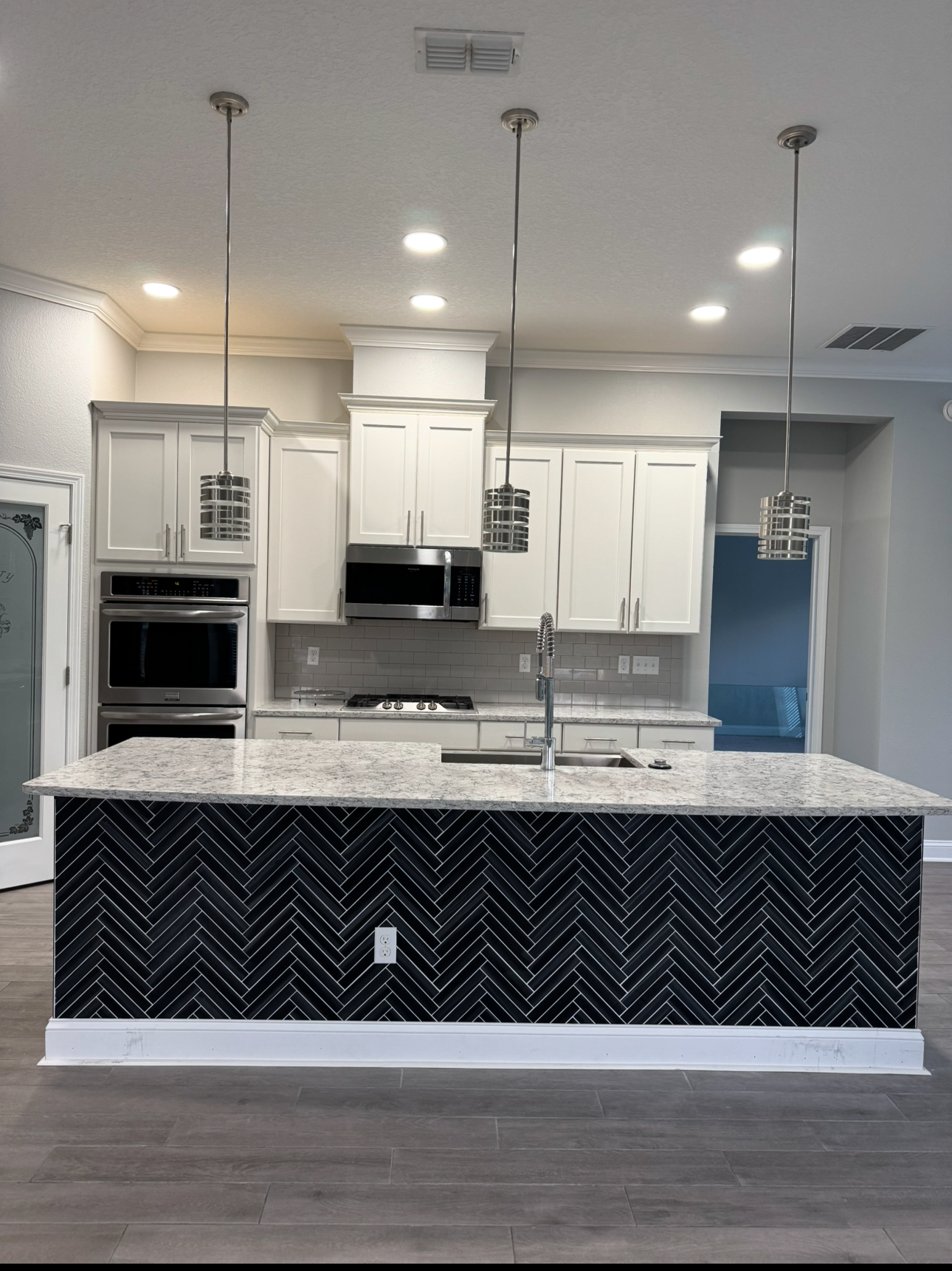 Modern kitchen with white cabinets, stainless steel appliances, granite countertops, and a black herringbone patterned island.