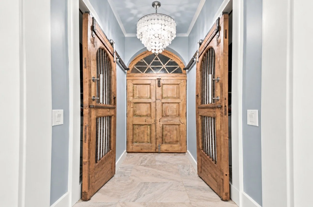 Rustic wood sliding barn doors flanking a hallway with arched wooden double doors, pale blue walls, and a chandelier