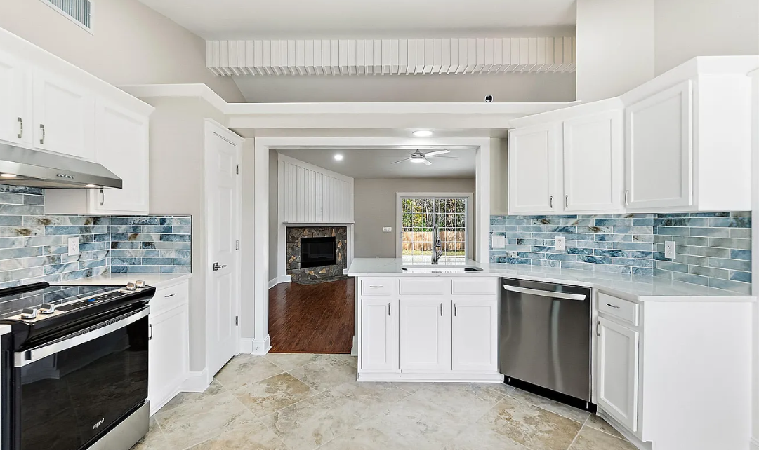 Modern kitchen with white cabinets, a gray tiled backsplash, stainless steel appliances including an oven, microwave, and stove, a granite countertop island with a black and white herringbone pattern on the front, and three pendant lights over the island.