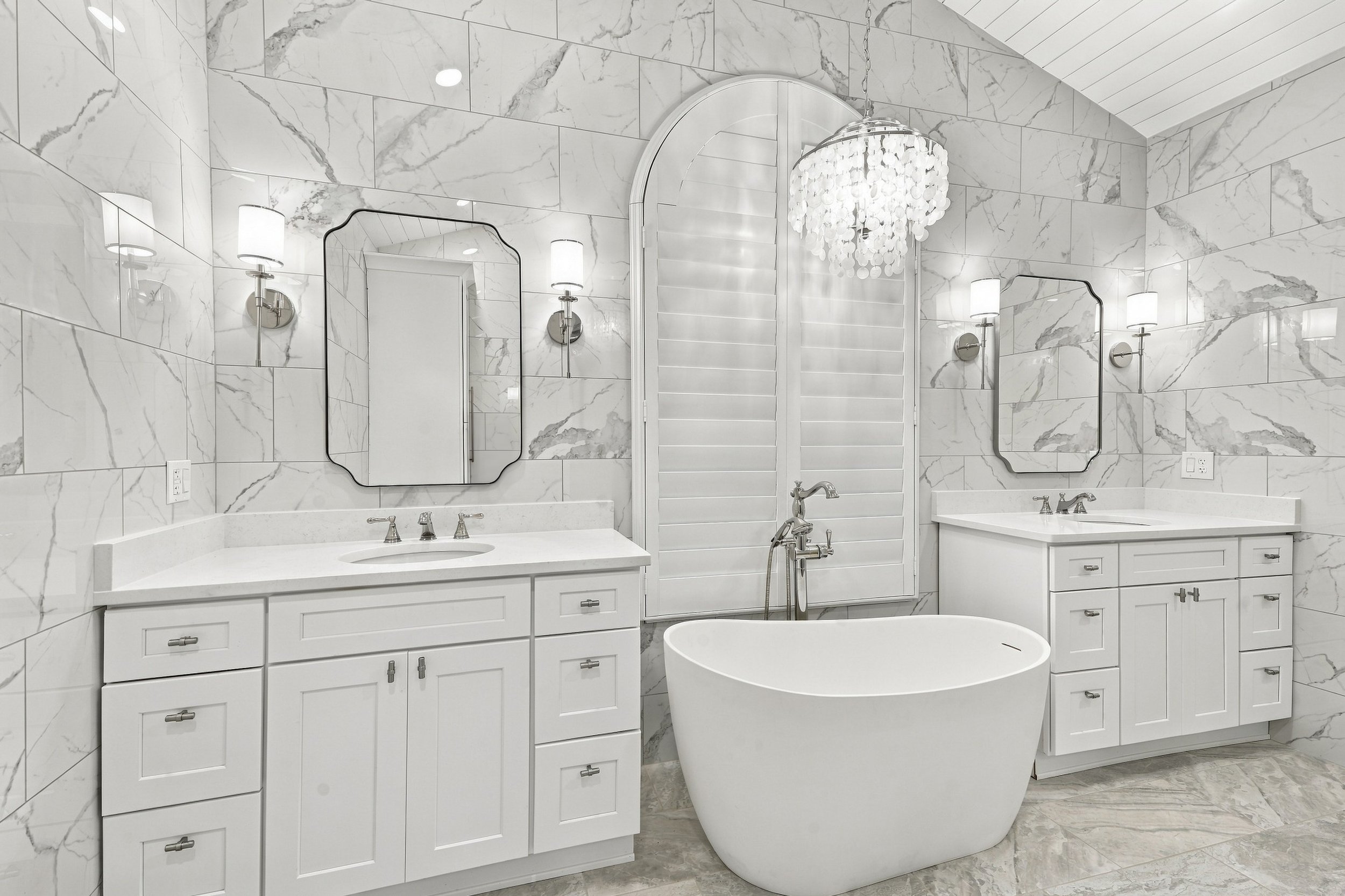 Bathroom featuring a white vanity with sink, mirror with lights, toilet, and a glass-enclosed shower with gray brick walls and a window.